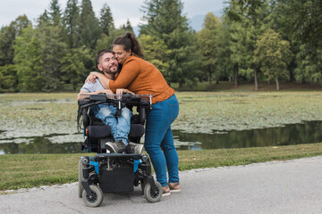 Man, an electric wheelchair user in the warm embrace of his wife, a couple enjoying and showing their affection. Disability and love concept.