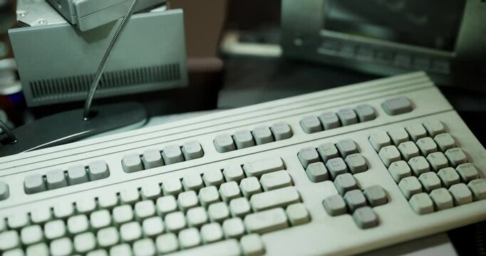 An old computer keyboard sits on a cluttered desk surrounded by various items. The keyboard shows signs of wear, indicating extensive use over time and capturing a nostalgic vibe.