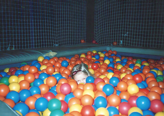 Circa 1990 - Brooklyn Park, Minnesota: Five year old child hides in a ball pit. Image is vintage and scanned, may have imperfections