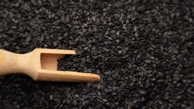 Black cumin seeds and wooden scoop, texture background