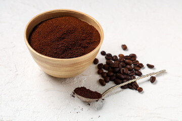 Wooden bowl of coffee powder with spoon and beans on white background