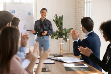Motivated staff members applauding young Indian female business trainer after successful...