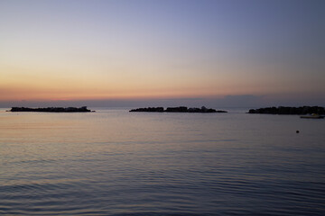 Naklejka premium Sun sinking into the horizon, breakwater at sunset, calm sea, calm scene with pink sky, reflecting sky in the sea, gentle waves in pastel colors, romantic view