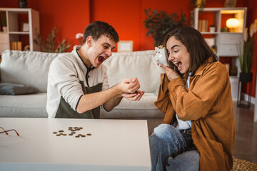 young excited woman hold piggy bank near head while man hold coins