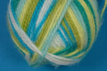 A close-up shot of a ball of yarn featuring a blend of green, blue, and white hues