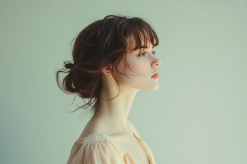 A young woman with brown hair in a messy bun, looking to the side against a muted green background.