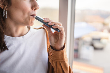 close up on woman smoking electronic cigar near window at home