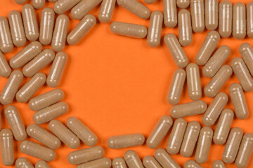 A top-down view of numerous beige capsules arranged in a circular pattern against a bright orange...
