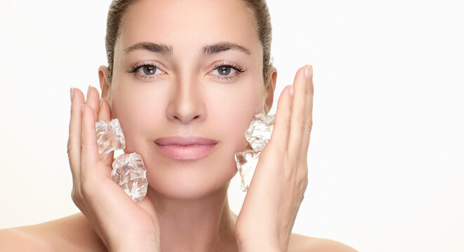 Woman applying ice cubes to her face for beauty and skincare routine against a white background