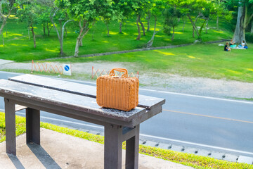 Rattan bag place on bench in outdoor for picnic day with green at park in summer,wicker basket,Fashionable handmade natural organic rattan bag.