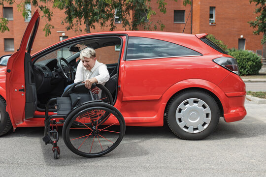 Smiling woman with disability sitting in the driver seat and lifting her wheelchair into the car, onto the front passenger seat.