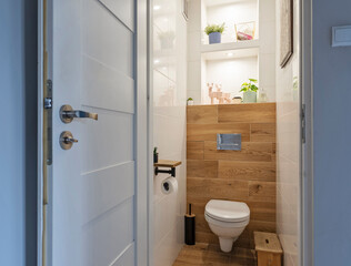 Rural bathroom with white tile and wooden tiles with led lights on shelf, stylish interior with toilet.