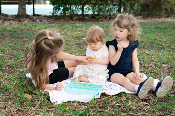 Sisters having a picnic outdoors, toddler and kids eating snacks on a blanket in the park