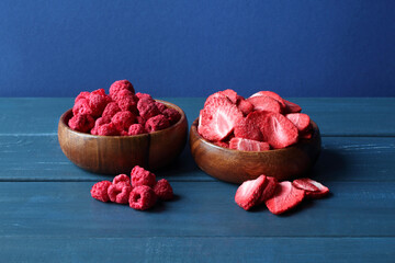 Dried raspberries and sliced dried strawberries in wooden bowls stand on blue wooden table. Closeup.