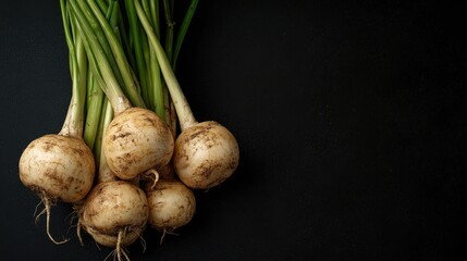 A bunch of fresh, round root vegetables with green tops against a dark background, showcasing their natural texture and earthy tones.