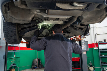 Serviceman checks car suspension on a column lift in car service.