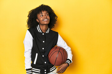 Vibrant teen girl with basketball on yellow studio background dreaming of achieving goals and...