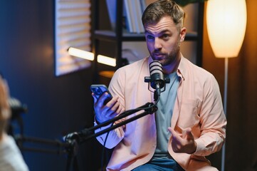 Man podcaster influencer blogger smiling while broadcasting his live audio podcast in studio using...