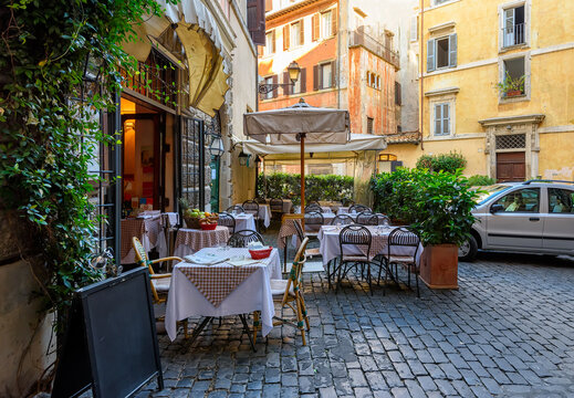 Fototapeta View of old narrow street with tables of restaurant in Rome, Italy. Architecture and landmark of Rome. Cozy cityscape of Rome.