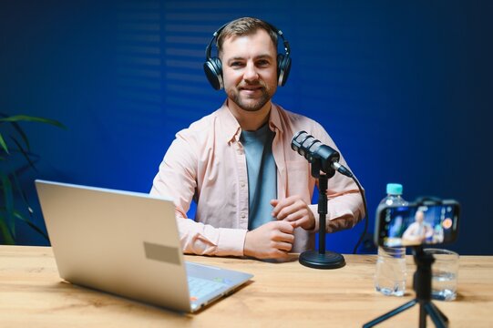 Man podcaster influencer blogger smiling while broadcasting his live audio podcast in studio using headphones. Male radio host making podcast or interview