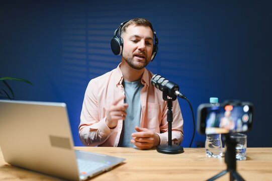 vlogger using smartphone to film podcast in studio. blogger with mobile phone, microphone and headphones filming video for social media broadcasting career