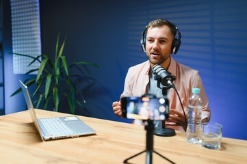Man podcaster influencer blogger smiling while broadcasting his live audio podcast in studio using...