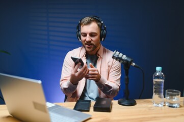 A video blogger records content in his studio. The host of the video blog is a young man who is...