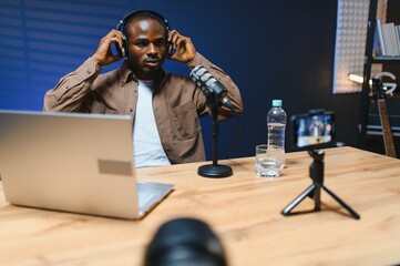 Black vlogger filming podcast on smartphone in studio. Cheerful blogger