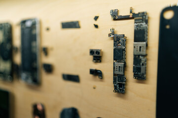 Disassembled smartphones displayed on wooden wall, exposing complex internal electronics and circuitry during professional technical diagnostic procedure in modern repair workshop, close-up