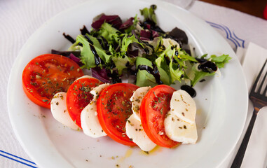 Mediterranean food, caprese salad - tomatoes, mozzarella cheese, dried basil and greens with balsamic on white plate