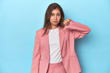 Teen girl in chic pink suit on a blue background showing a dislike gesture, thumbs down....