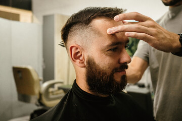 Obraz premium Barbershop. Unrecognizable male barber hands making customer Fashionable haircut in Modern style barber shop. Bearded Man client visit gentleman grooming beauty salon for hairstyle care