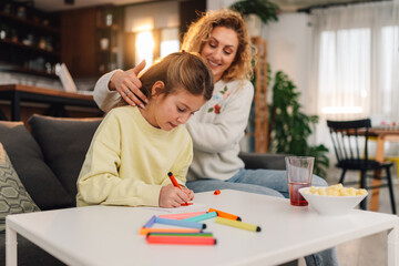 Girl drawing mother's day card with her mother caressing her hair