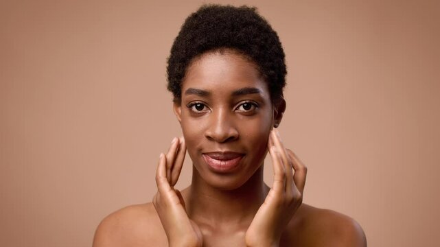 A young African American woman with short hair expresses herself, touching her face in a minimalistic setting. The focus showcases her features and confidence, offering an intimate vibe.