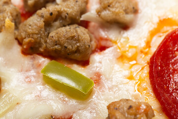Slice of fresh Italian classic original sausage and pepperoni supreme pizza with green pepper and cheese on a white glossy plate