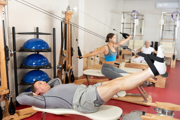 Adult man in sportswear training her legs with straps in pilates studio..