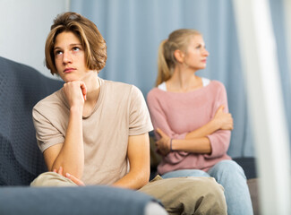 Obraz premium Portrait of unhappy teenage son after discord with mother sitting at sofa indoors