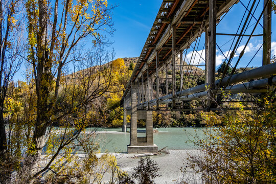 Historic Lower Shotover Bridge with ts impressive steel and concrete construction against vibrant autumn trees and the glacial waters of the Shotover River near Queenstown, New Zealand.