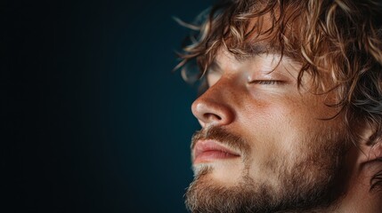 Fototapeta premium A serene close-up portrait of a young man with curly hair and a beard, showcasing tranquility and deep emotion as he enjoys a moment of calm existence.