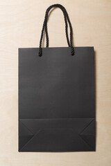 Recyclable black paper shopping bag on a birch wood panel background with a black fabric braided handle. can be used for a mockup for design