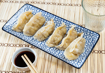On tablecloth of straw-mat is plate with portion of boiled gyoza dumplings, bowl of soy sauce and chopsticks. Traditional oriental culinary art, acquaintance with culture through national cuisine