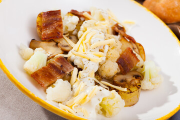 Tasty baked potatoes with garnish of cauliflower, fried bacon and mushrooms with cheese dip sauce