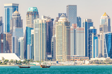 Obraz premium Doha modern business downtown center skyscrapers shoreline with small traditional arab dhow fishermen boats at the sea bay, Qatar