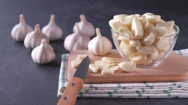 Chopped garlic on a cutting board, in  black stone table a pile of garlic unpeeled.