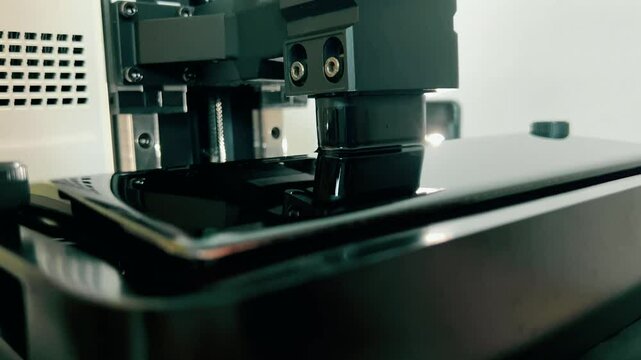 Rising build platform with dripping transparent red photopolymer or photosensitive resin in a modern SLA 3D printer, close-up