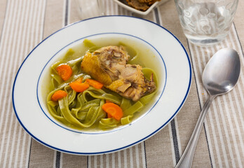 Hot and hearty soup is traditional Russian dish in plate. Chicken broth with long green noodles, decorated with carrot slices
