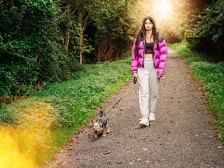 Young teenager girl with her small cute Yorkshire terrier on a walk in a forest park. Taking care of your pet theme. Model has slim body type and long rich hair. Selective focus.