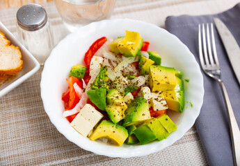 Fresh avocado, tomato, onion salad served in white circular plate.