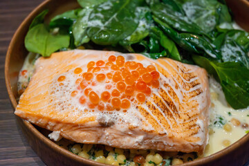Portion of grilled wild scottish salmon served with green spinach and white cream sauce and red caviar