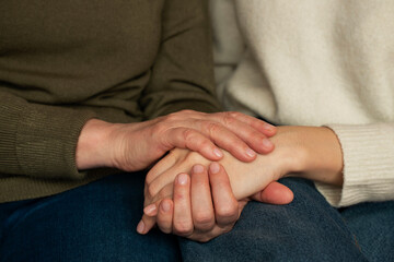 A daughter and mother embrace each other hands after a long separation, sitting close, sharing a...